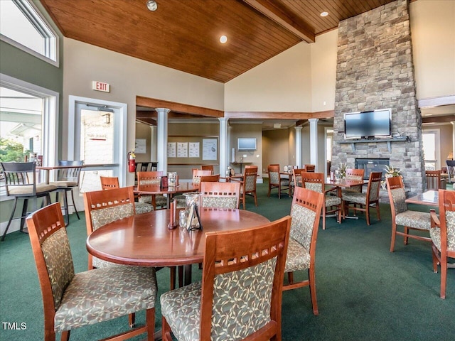 dining space with a stone fireplace, ornate columns, wood ceiling, high vaulted ceiling, and carpet floors