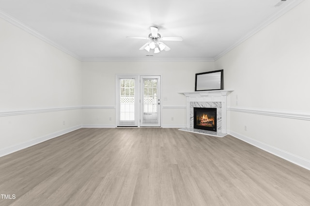 unfurnished living room with a premium fireplace, ornamental molding, ceiling fan, and light hardwood / wood-style flooring