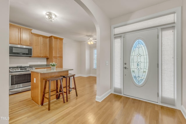 foyer featuring a ceiling fan, arched walkways, baseboards, and light wood finished floors