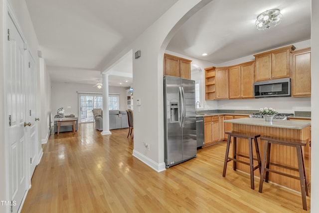 kitchen featuring a breakfast bar area, a sink, light countertops, appliances with stainless steel finishes, and open shelves