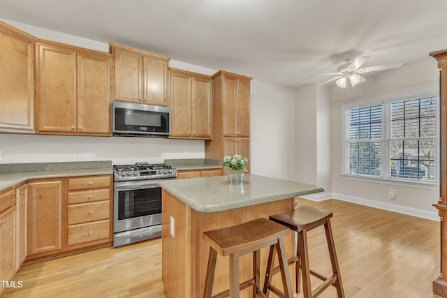 kitchen featuring ceiling fan, stainless steel appliances, a kitchen island, a kitchen breakfast bar, and light wood finished floors