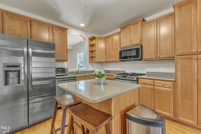 kitchen featuring appliances with stainless steel finishes, a kitchen breakfast bar, light wood-style floors, open shelves, and a sink