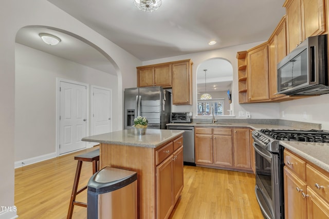 kitchen with a center island, a breakfast bar, open shelves, stainless steel appliances, and a sink