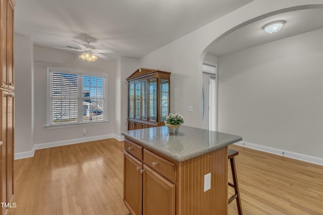 kitchen with a breakfast bar, arched walkways, a center island, and light wood-type flooring