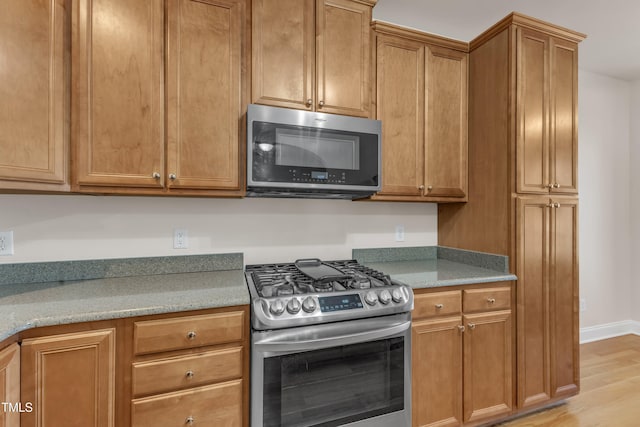 kitchen with stainless steel appliances, brown cabinets, light wood-style floors, and light stone counters