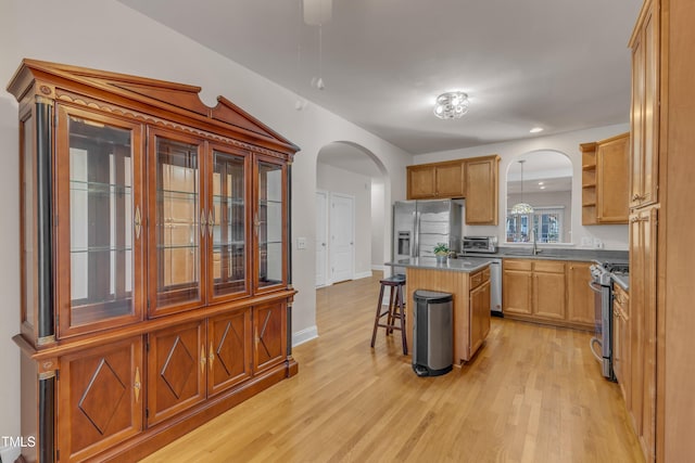 kitchen with a center island, arched walkways, hanging light fixtures, appliances with stainless steel finishes, and a kitchen breakfast bar