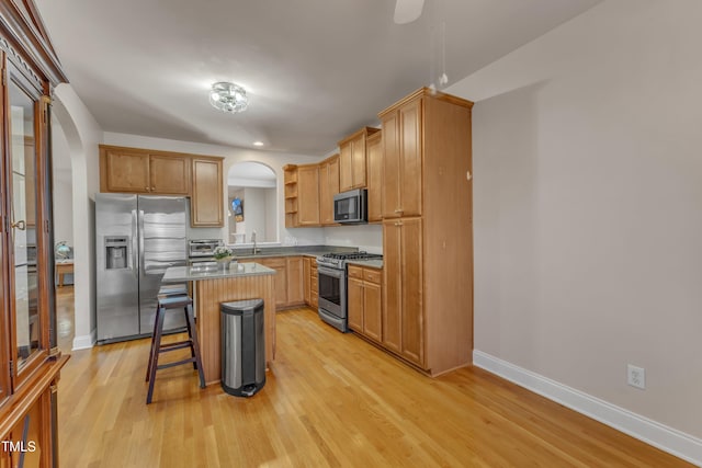 kitchen featuring a center island, arched walkways, a breakfast bar, open shelves, and appliances with stainless steel finishes