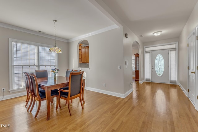 dining room featuring arched walkways, light wood finished floors, crown molding, and baseboards