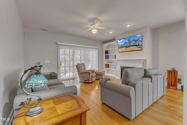 living room featuring ceiling fan, a fireplace, light wood-style flooring, and built in features