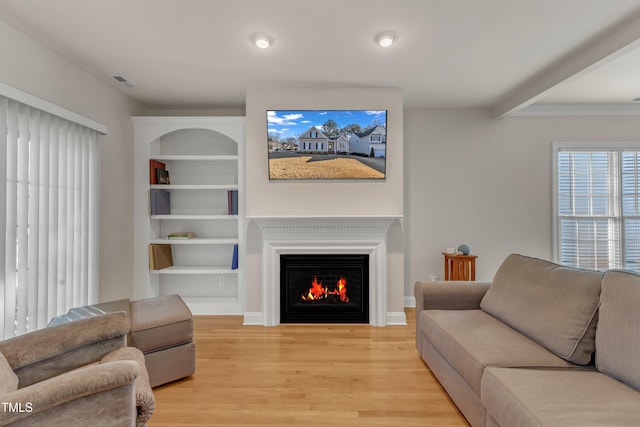 living room featuring a warm lit fireplace, visible vents, baseboards, built in features, and light wood-style floors