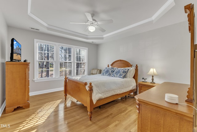 bedroom with baseboards, a raised ceiling, visible vents, and light wood-style floors