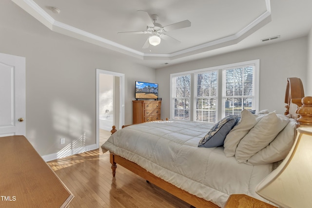 bedroom with baseboards, visible vents, a raised ceiling, ornamental molding, and light wood-type flooring