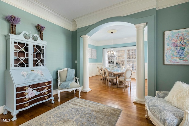 sitting room featuring crown molding, a notable chandelier, hardwood / wood-style flooring, and ornate columns