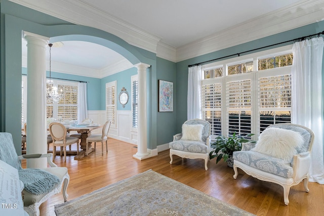 living area featuring hardwood / wood-style flooring, crown molding, an inviting chandelier, and ornate columns