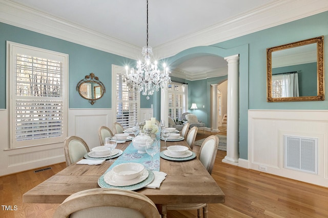 dining room with hardwood / wood-style flooring, ornamental molding, decorative columns, and a notable chandelier