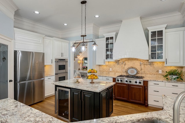 kitchen with wine cooler, custom exhaust hood, hanging light fixtures, appliances with stainless steel finishes, and a kitchen island