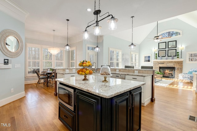 kitchen with a kitchen island with sink, hanging light fixtures, stainless steel microwave, and light stone countertops