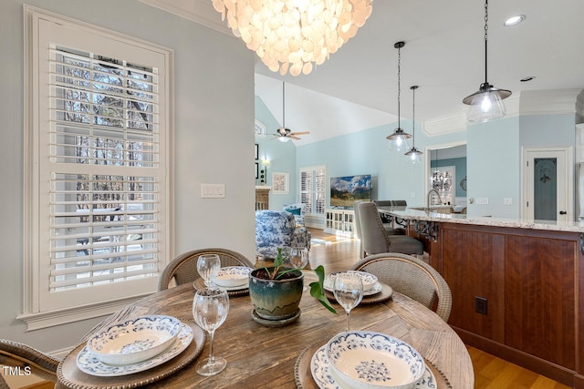 dining area with ornamental molding, vaulted ceiling, ceiling fan with notable chandelier, and light wood-type flooring