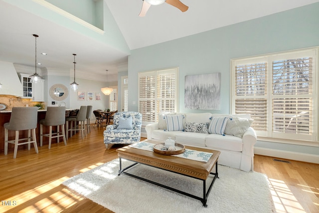 living room with ceiling fan, high vaulted ceiling, ornamental molding, and light wood-type flooring