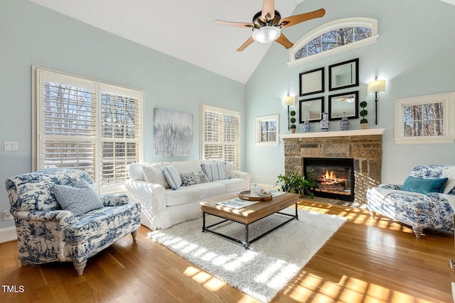 living room featuring a stone fireplace, wood-type flooring, high vaulted ceiling, and ceiling fan