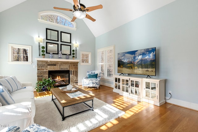 living room featuring ceiling fan, wood-type flooring, a stone fireplace, and high vaulted ceiling