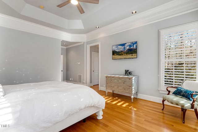 bedroom with hardwood / wood-style flooring, crown molding, ceiling fan, and a tray ceiling