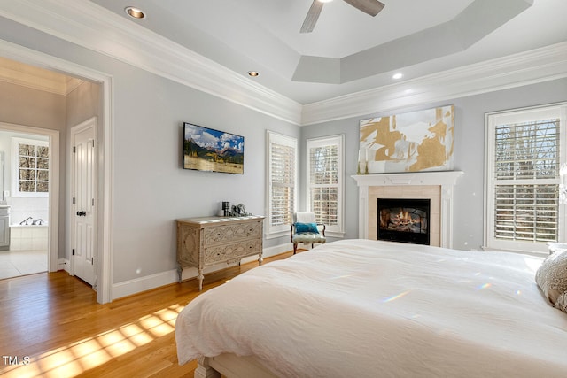 bedroom featuring hardwood / wood-style floors, a tray ceiling, a fireplace, and ornamental molding