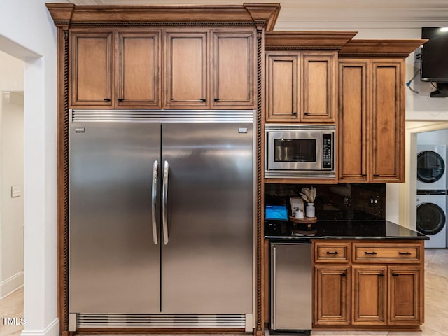 kitchen featuring light tile patterned flooring, dark stone countertops, backsplash, stacked washer and dryer, and built in appliances