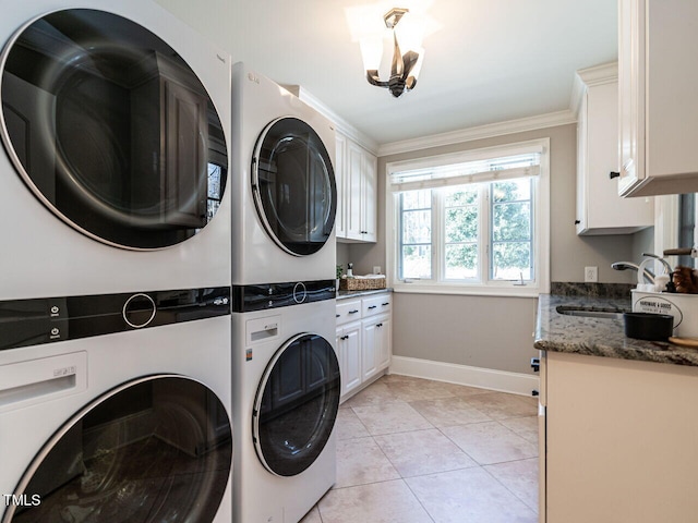 clothes washing area featuring sink, light tile patterned floors, stacked washing maching and dryer, cabinets, and ornamental molding