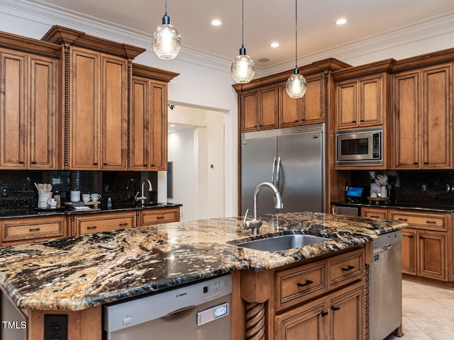 kitchen with sink, built in appliances, decorative light fixtures, a center island with sink, and dark stone counters