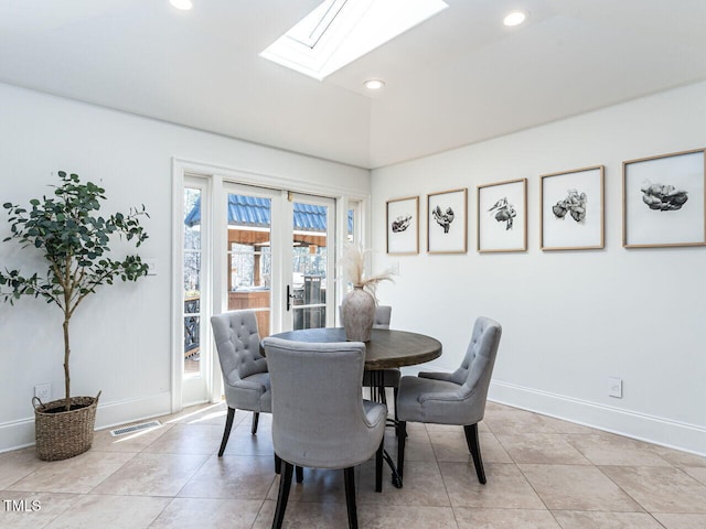 dining space with light tile patterned flooring and vaulted ceiling with skylight