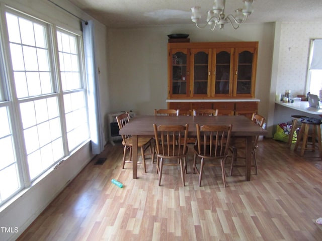dining area featuring a chandelier, a healthy amount of sunlight, light wood-style flooring, and wallpapered walls