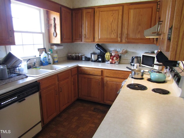 kitchen with brown cabinetry, dishwasher, light countertops, a sink, and exhaust hood
