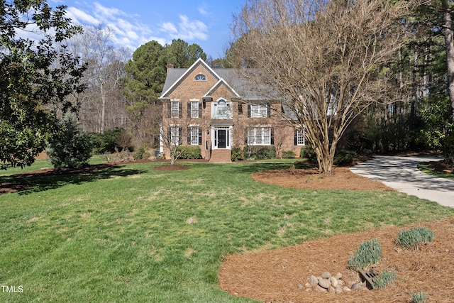 view of front of home with brick siding, a chimney, and a front lawn