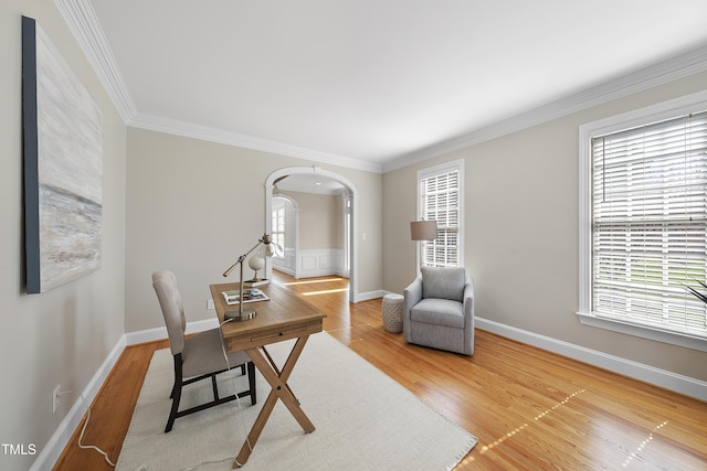 home office featuring crown molding, baseboards, arched walkways, and light wood finished floors