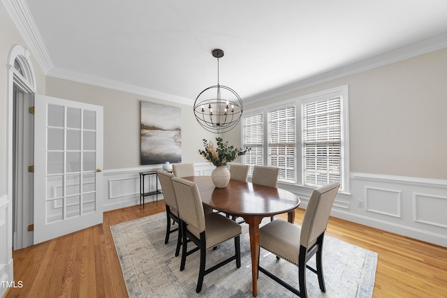 dining space with crown molding, a wainscoted wall, light wood-type flooring, an inviting chandelier, and a decorative wall