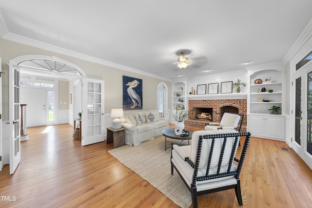 living area with a fireplace, light wood-style flooring, built in features, and french doors