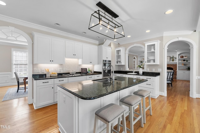 kitchen with arched walkways, light wood finished floors, a breakfast bar area, and a sink