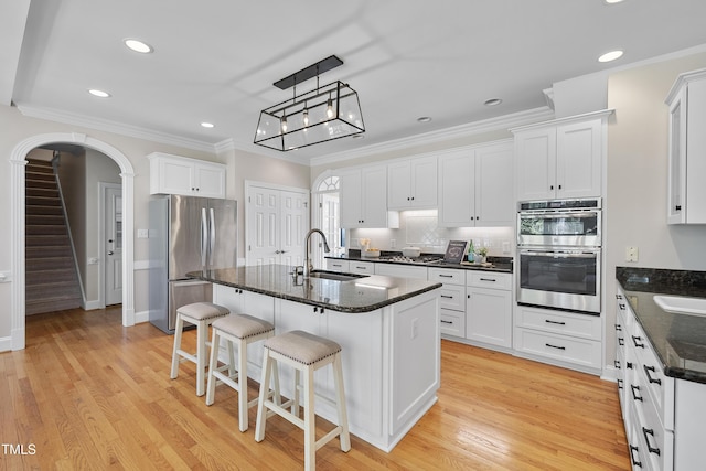 kitchen with a sink, arched walkways, appliances with stainless steel finishes, crown molding, and light wood finished floors