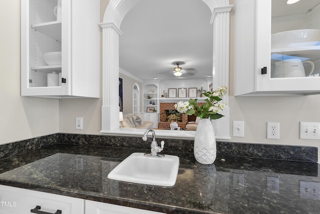 interior space with a brick fireplace, decorative columns, ceiling fan, and a sink