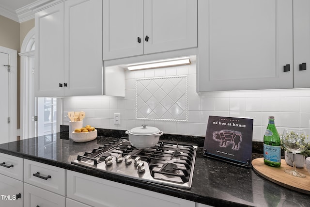 kitchen with backsplash, crown molding, stainless steel gas cooktop, dark stone countertops, and white cabinets