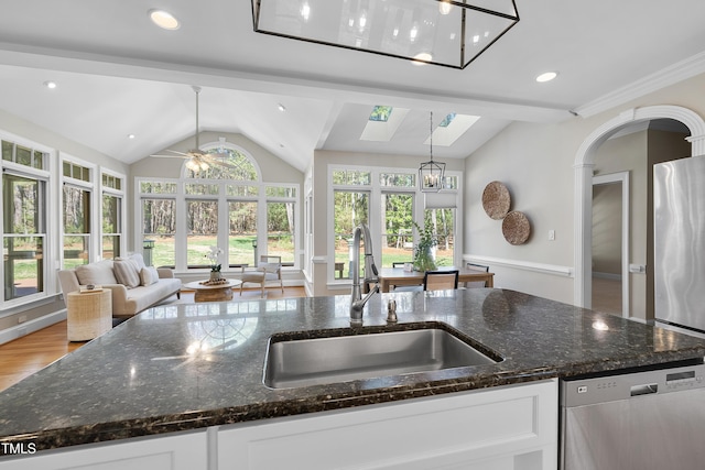 kitchen with a sink, white cabinets, open floor plan, and stainless steel dishwasher