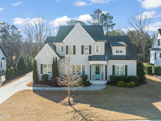 view of front facade featuring roof with shingles, a front yard, a standing seam roof, metal roof, and driveway