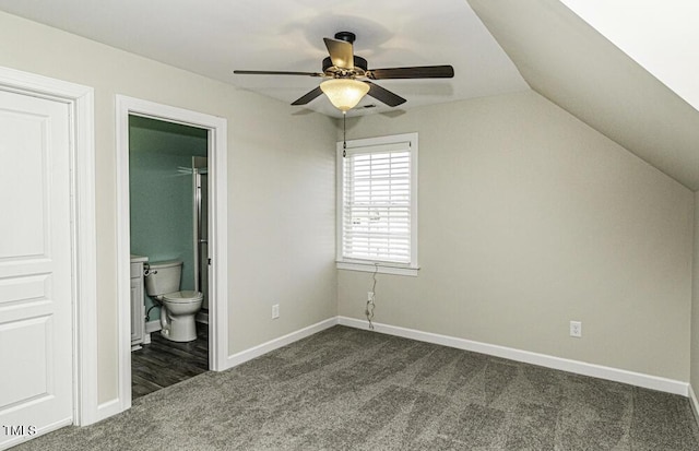 unfurnished bedroom featuring lofted ceiling, dark carpet, ensuite bath, and ceiling fan