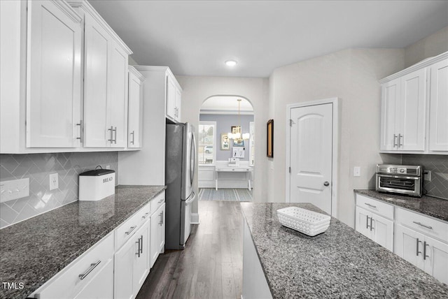 kitchen with dark wood-type flooring, white cabinetry, tasteful backsplash, stainless steel fridge, and dark stone counters