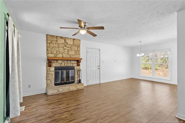 unfurnished living room with wood-type flooring, a stone fireplace, ceiling fan with notable chandelier, and a textured ceiling