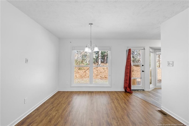 unfurnished dining area with hardwood / wood-style flooring, a notable chandelier, and a textured ceiling