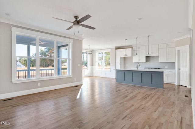 kitchen with white cabinetry, crown molding, a kitchen island with sink, and pendant lighting