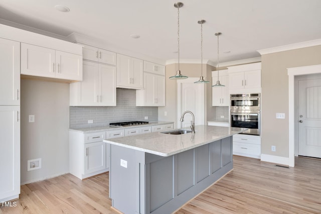 kitchen with a center island with sink, white cabinetry, sink, and pendant lighting