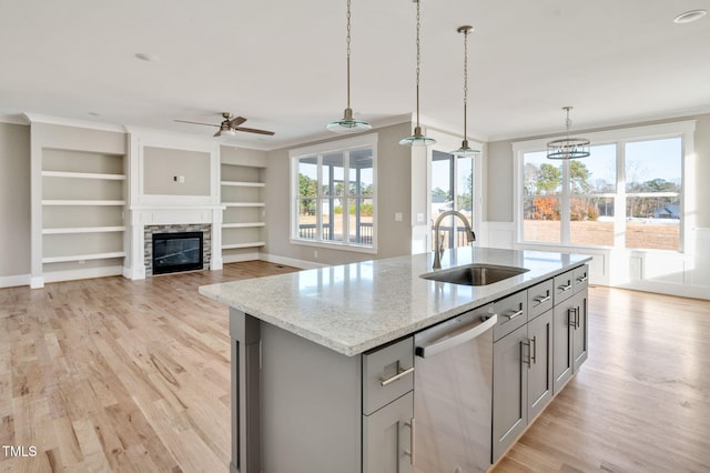 kitchen featuring pendant lighting, sink, dishwasher, light stone counters, and a center island with sink